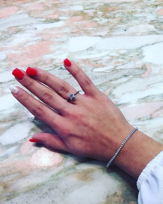 Una mano appoggiata sul marmo con un anello a una pietra e un bracciale di pietre chiare