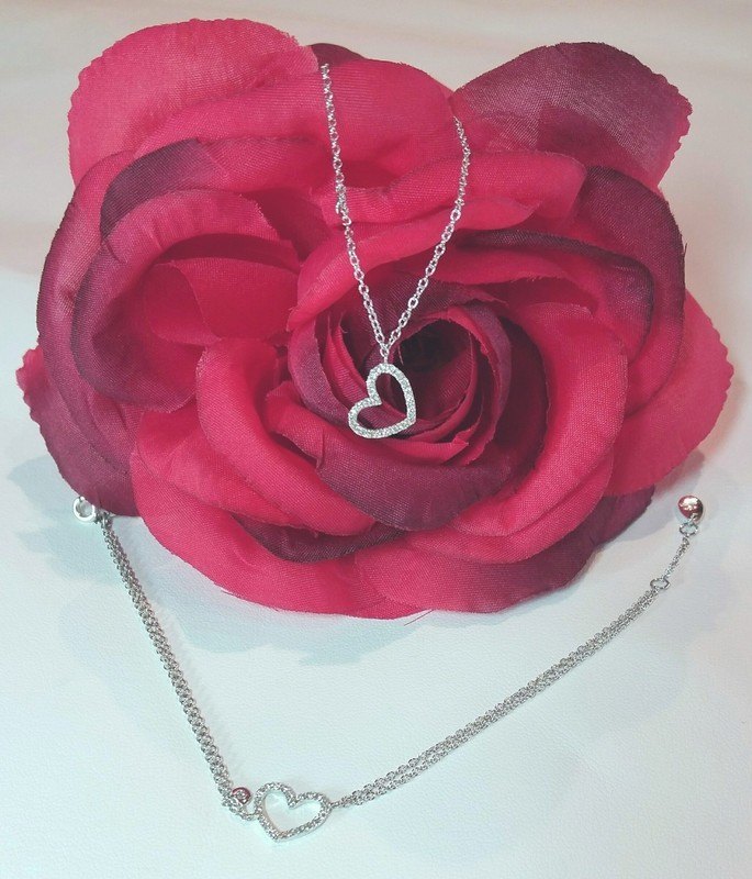Una collana con ciondolo a cuore e un bracciale con un cuore, appoggiati su una rosa rossa